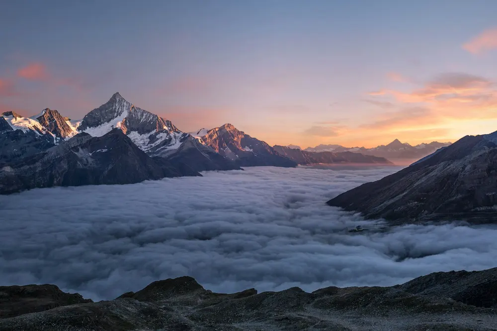 Jagged mountain peaks rising above a sea of clouds at sunrise